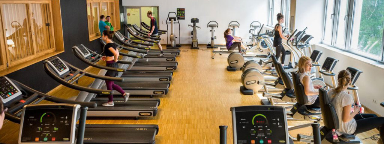 BME kampüsündeki modern spor salonunda spor ekipmanlarını kullanan öğrencilerin yer aldığı geniş ve aydınlık bir fitness alanı.